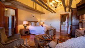A cozy bedroom with a wooden ceiling, a large bed, bedside lamps, and a small table with decorative items. - Magic Hills - Ilanga Manor House (Ikwezi)