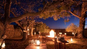 An outdoor dining area with tables and chairs, surrounded by trees and stone walls. - Magic Hills - Ilanga Manor House (Ikwezi)