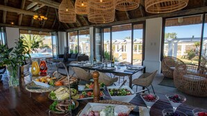 A dining area with a buffet setup, wicker chairs, and a view of the outdoors. - Magic Hills - Ilanga Manor House (Ikwezi)