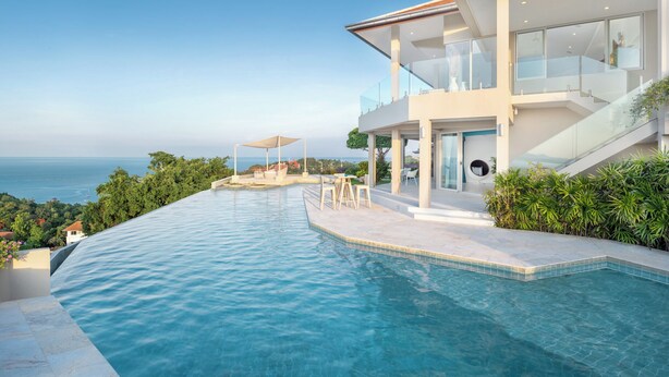 Een modern huis met een groot overloopzwembad met uitzicht op zee.