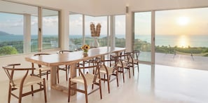 Enjoy meals with a view of the sea and distant hills from this dining area with a long table and six chairs.
