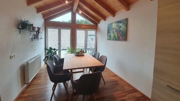 Un comedor con mesa y sillas de madera, ventanas amplias y vistas al exterior.