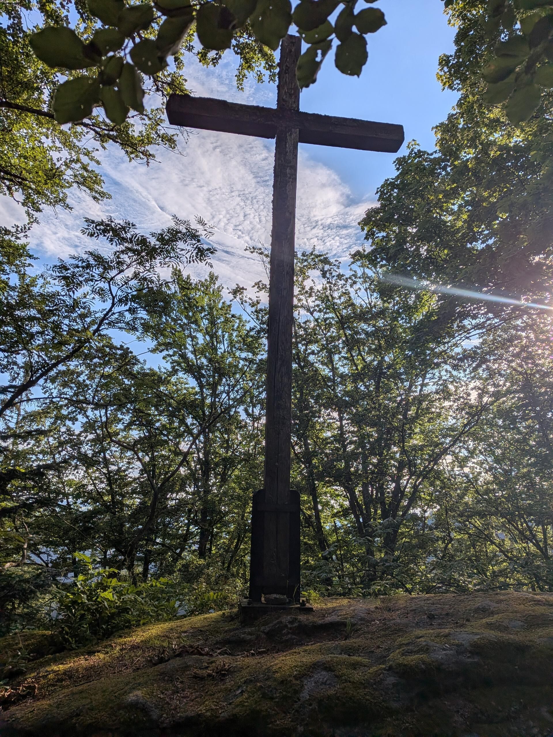 A cross in a forested area with sunlight filtering through the trees.