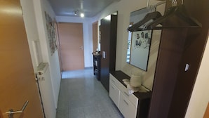 Un pasillo con una puerta de madera a la izquierda, un radiador blanco, un armario de madera oscura con un espejo y un perchero.