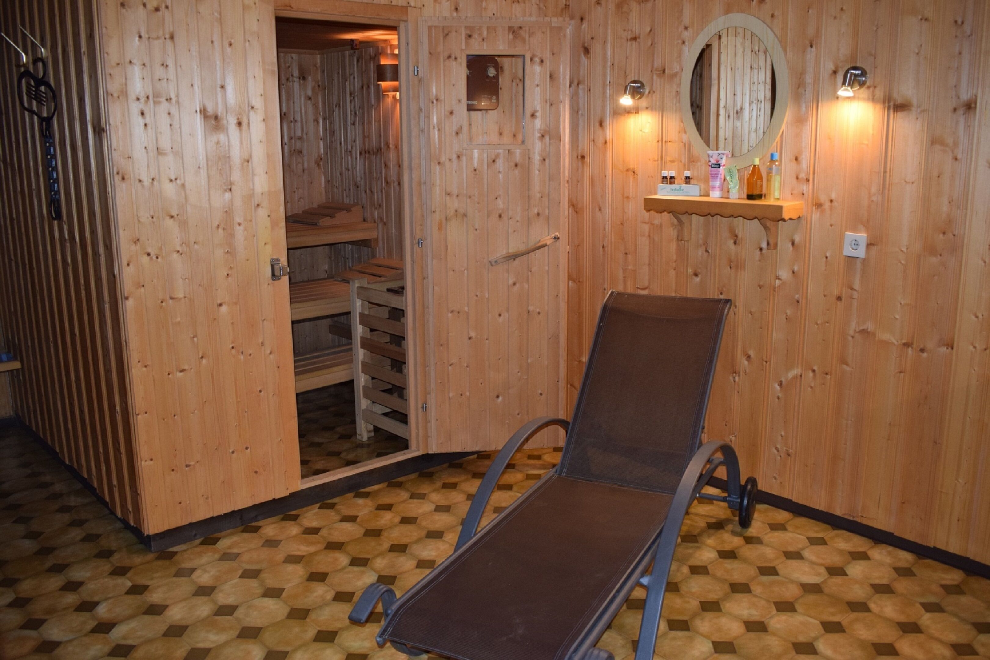 A wooden sauna room with a single reclining chair, a shelf with personal items, and a mirror on the wall.