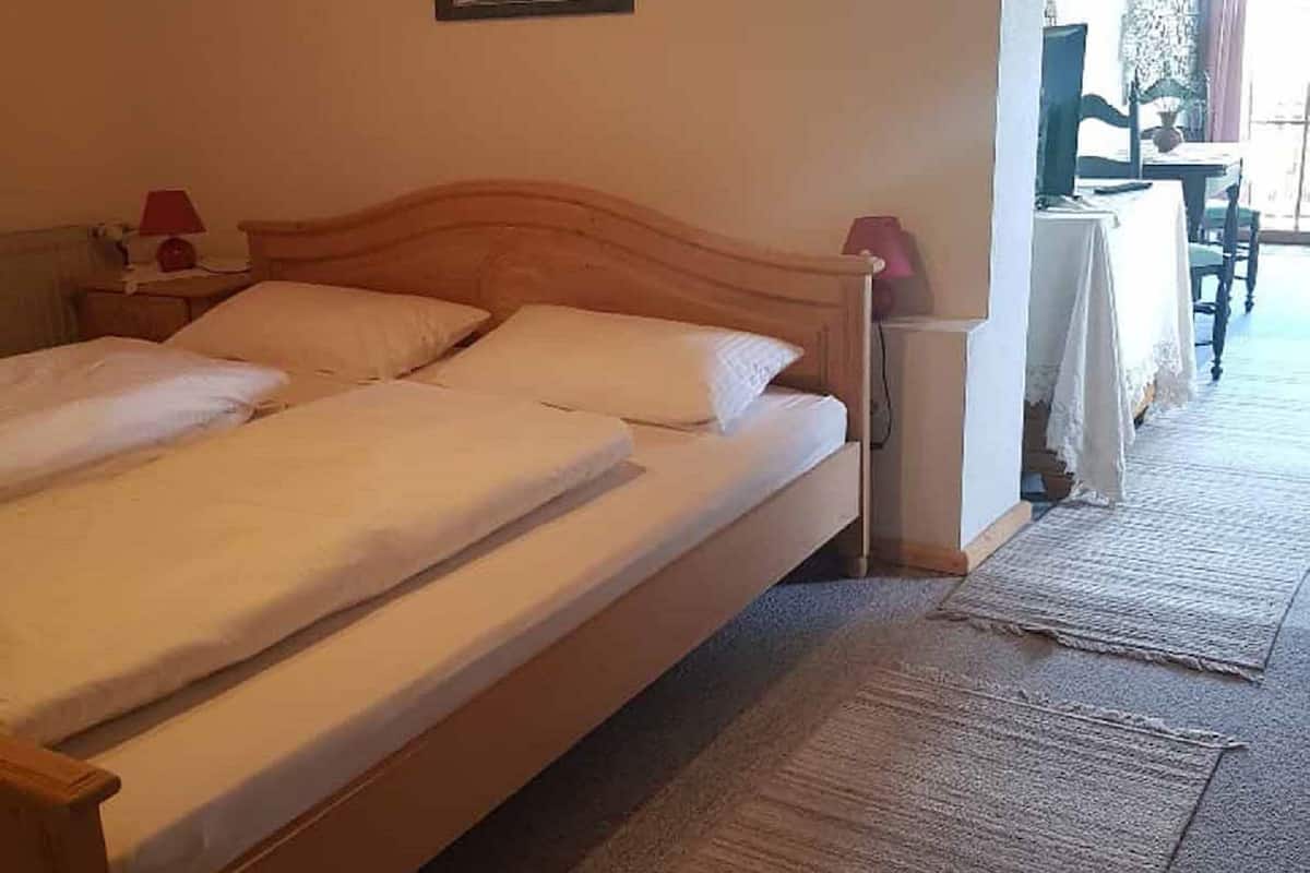 A room with a large bed, a small bedside table with a lamp, a chair, and a table with a tablecloth.
