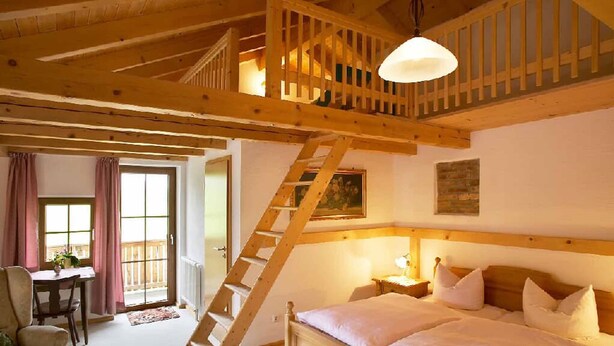 A bedroom with a wooden ladder leading to a loft, a bed with white bedding, a nightstand, and a window with curtains. - Landgasthof Vogl - Zum Klement (Neukirchen Beim Heiligen Blut)