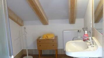 A small bathroom with a white sink, wooden beams, a yellow towel, and a blue trash bin.