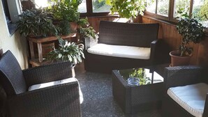 A cozy patio area with wicker furniture, including a sofa and chairs, surrounded by potted plants. - Landgasthof Vogl - Zum Klement (Neukirchen Beim Heiligen Blut)