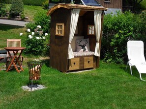 Uma cabana de madeira com um banco e uma mesa, rodeada por vegetação.