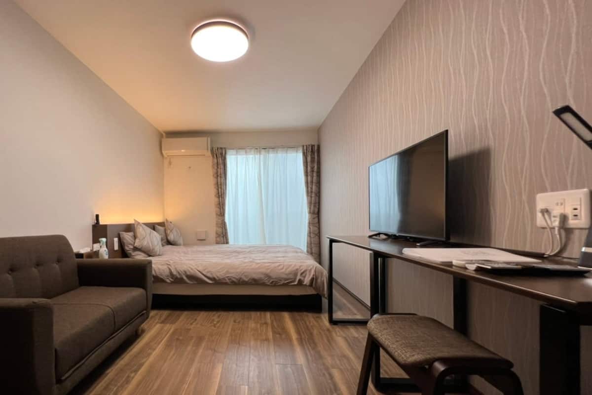 Una habitación de hotel moderna con una cama, un sofá, un escritorio con televisor y un taburete pequeño.