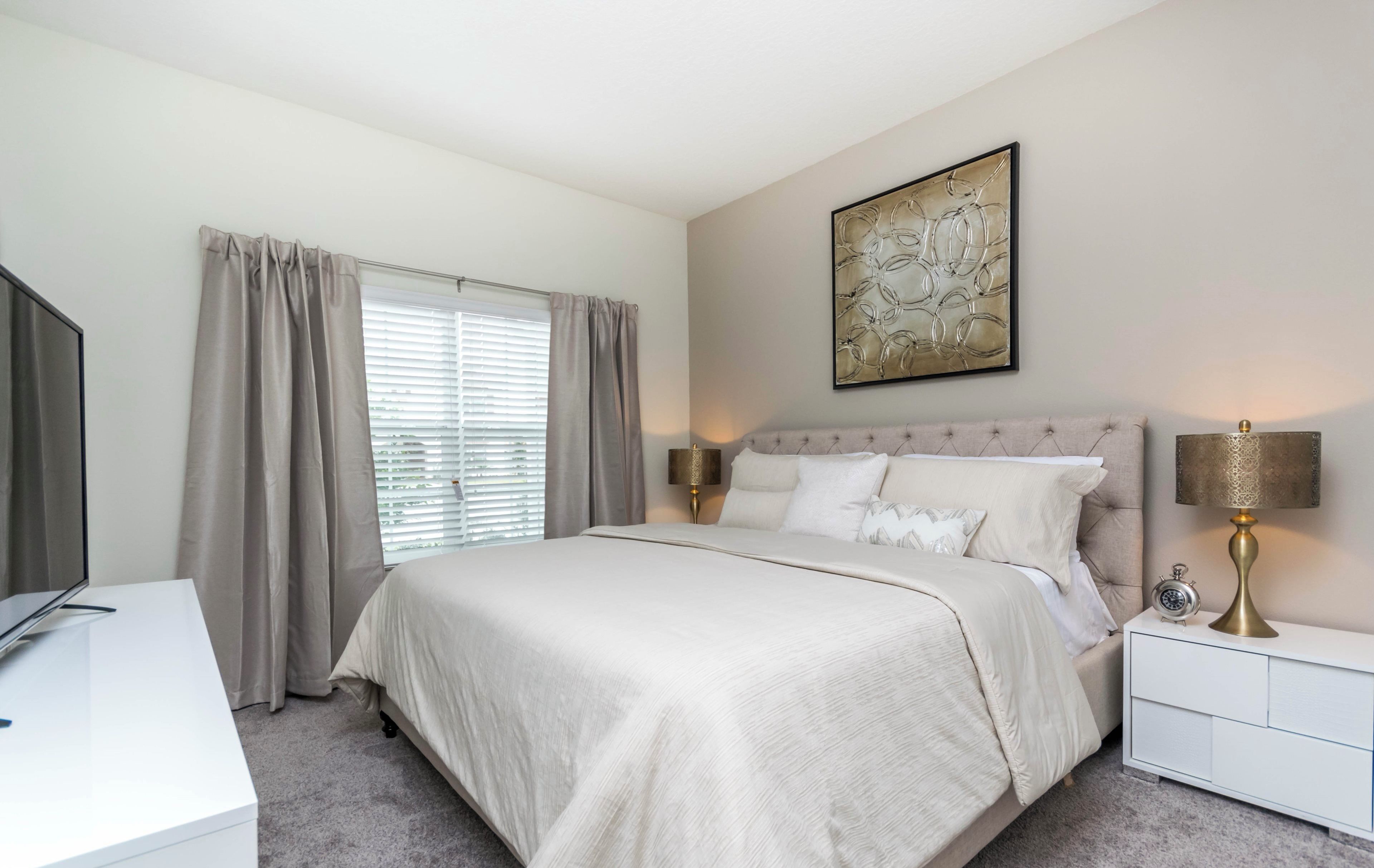 Een slaapkamer met een groot bed, twee nachtkastjes, een lamp, een klok en een raam met gordijnen.
