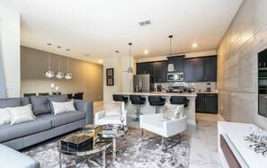 A modern living room with a grey sofa, a white armchair, and a glass coffee table. - Private Splash Pool • Lazy River • Golf • 12 Miles to Disney (Davenport)