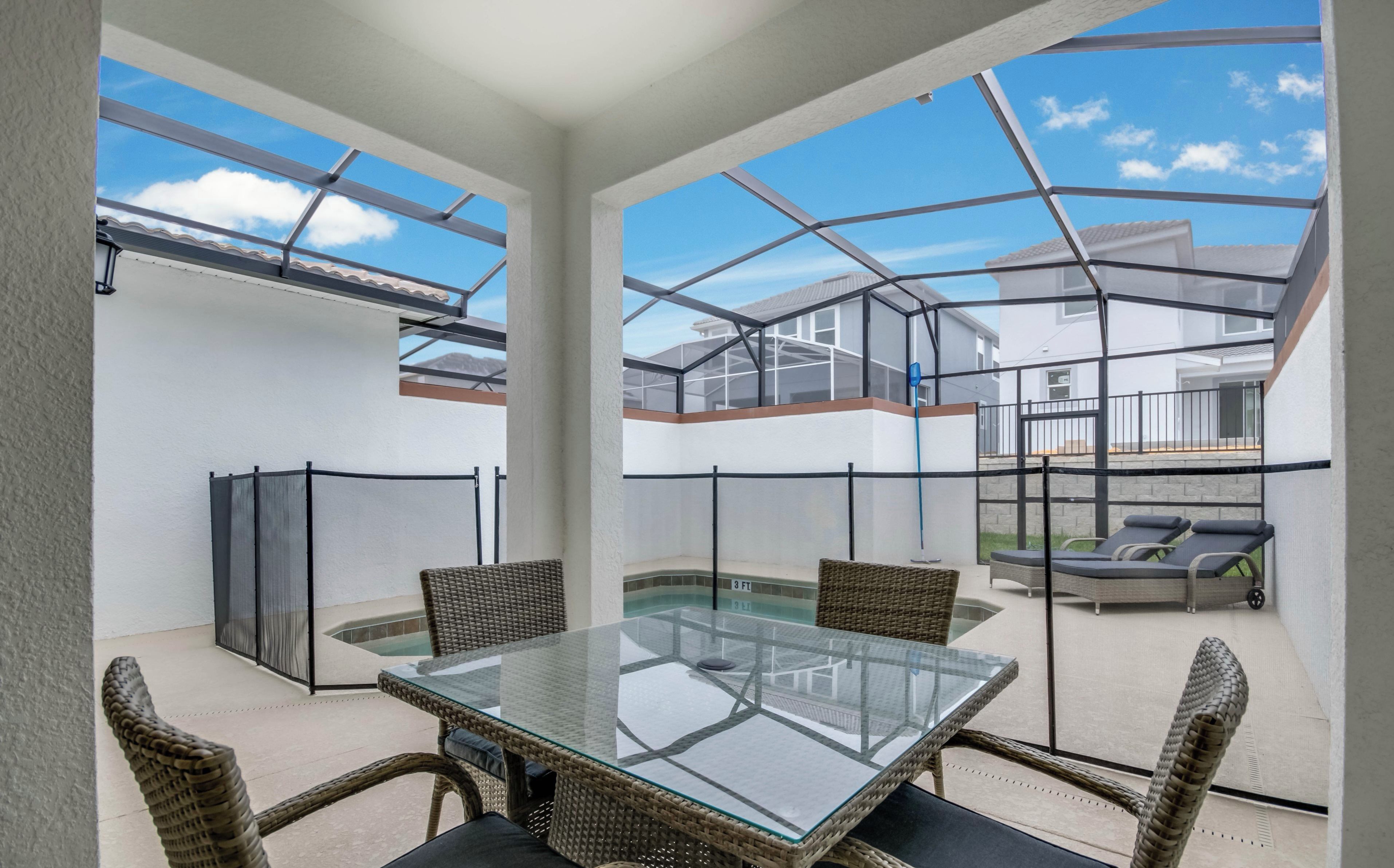 Ein Tisch mit Glasplatte, Korbstühle, eine überdachte Terrasse aus Glas und Blick auf benachbarte Häuser.