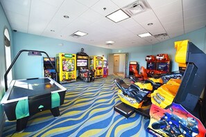 A room with a pool table, arcade games, and a motorcycle simulator.