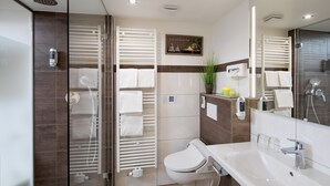 Et moderne badeværelse med brusekabine i glas, toilet, vask med spejl og et håndklædestativ.
