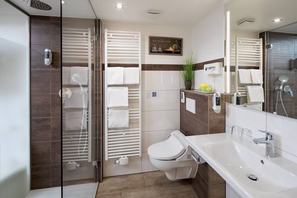 A modern bathroom with a glass shower enclosure, a toilet, a sink with a mirror, and a towel rack.