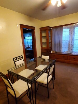 A dining area with a glass-top table and four chairs, a wooden cabinet, and a window with curtains. - Cozy 2-bedroom in Cleveland (Cleveland)