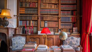 A library with bookshelves, a desk with books, a globe, and a red lamp. - Domaine de Chalaniat (La Sauvetat)