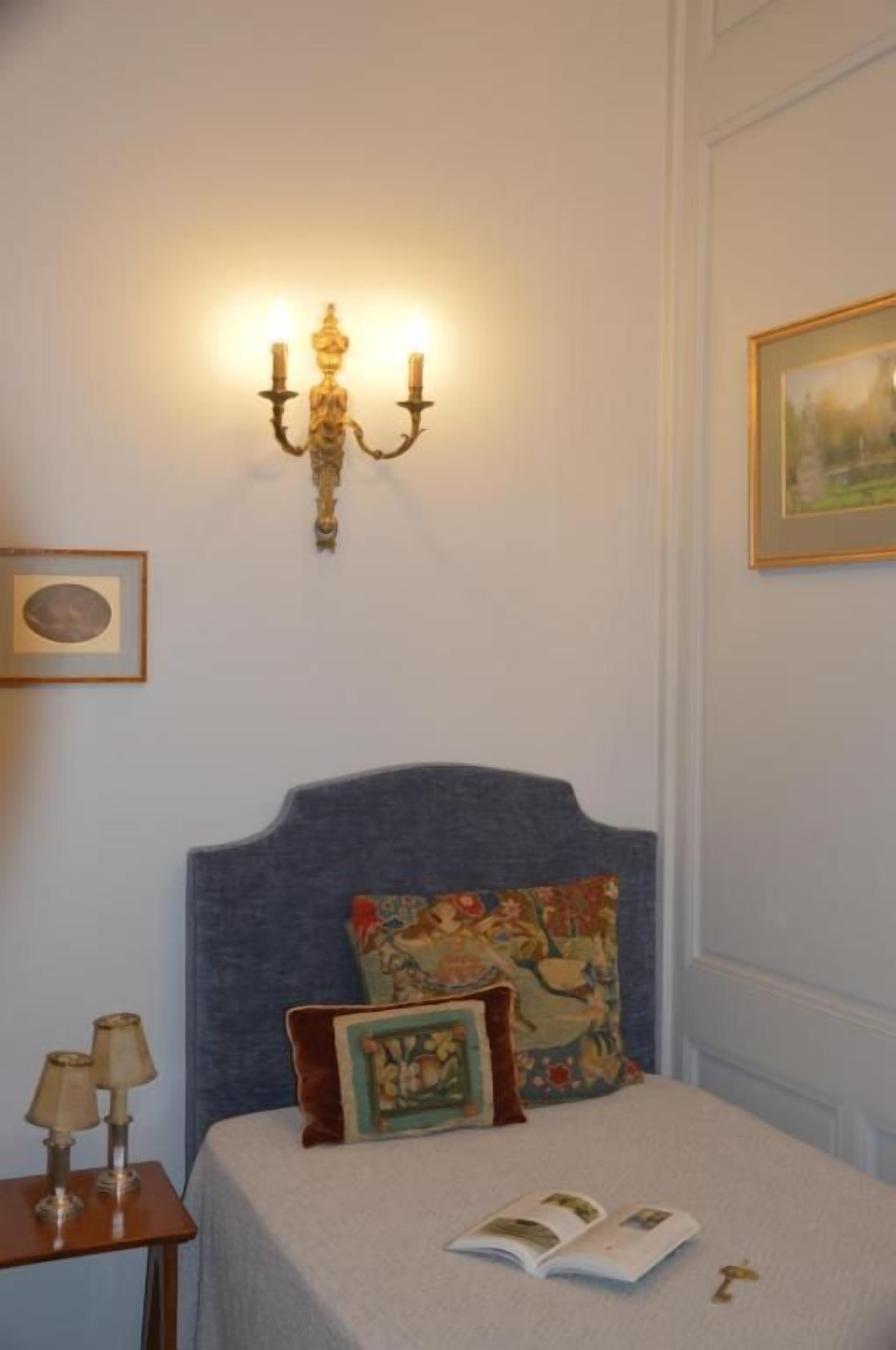 Een slaapkamer met een bed, een wandlamp en een ingelijst kunstwerk.