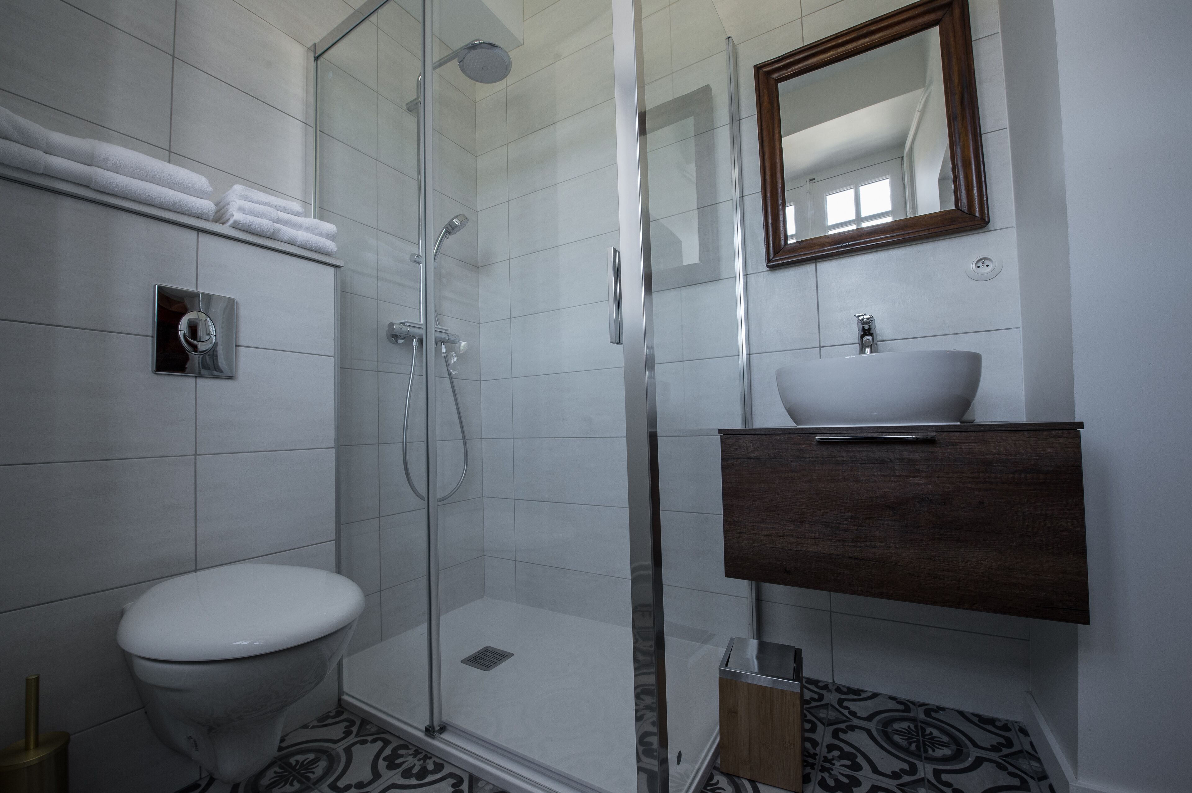 Un baño moderno con ducha envuelta en vidrio, inodoro blanco y tocador de madera con lavamanos.