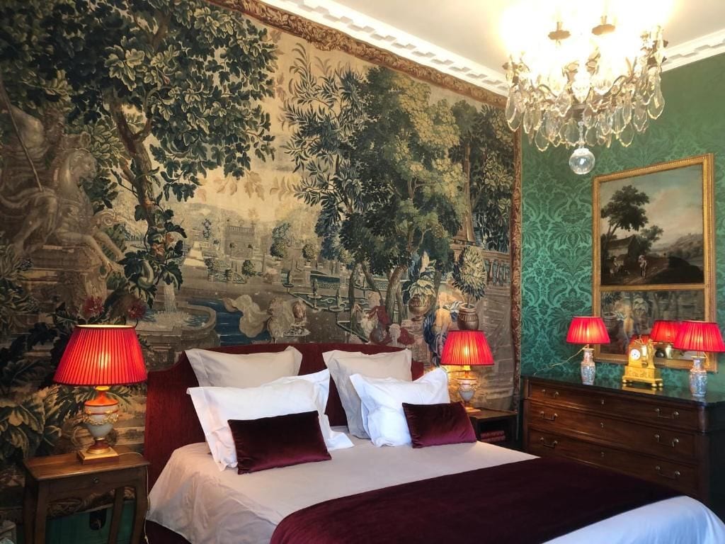 Hotellihuone, jossa on suuri sänky, kaksi yöpöytää, kattokruunu ja seinämaalaus.