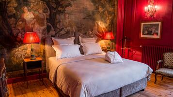 A large bed with white linens, two bedside tables with lamps, a red wall with a mural, and a chair.