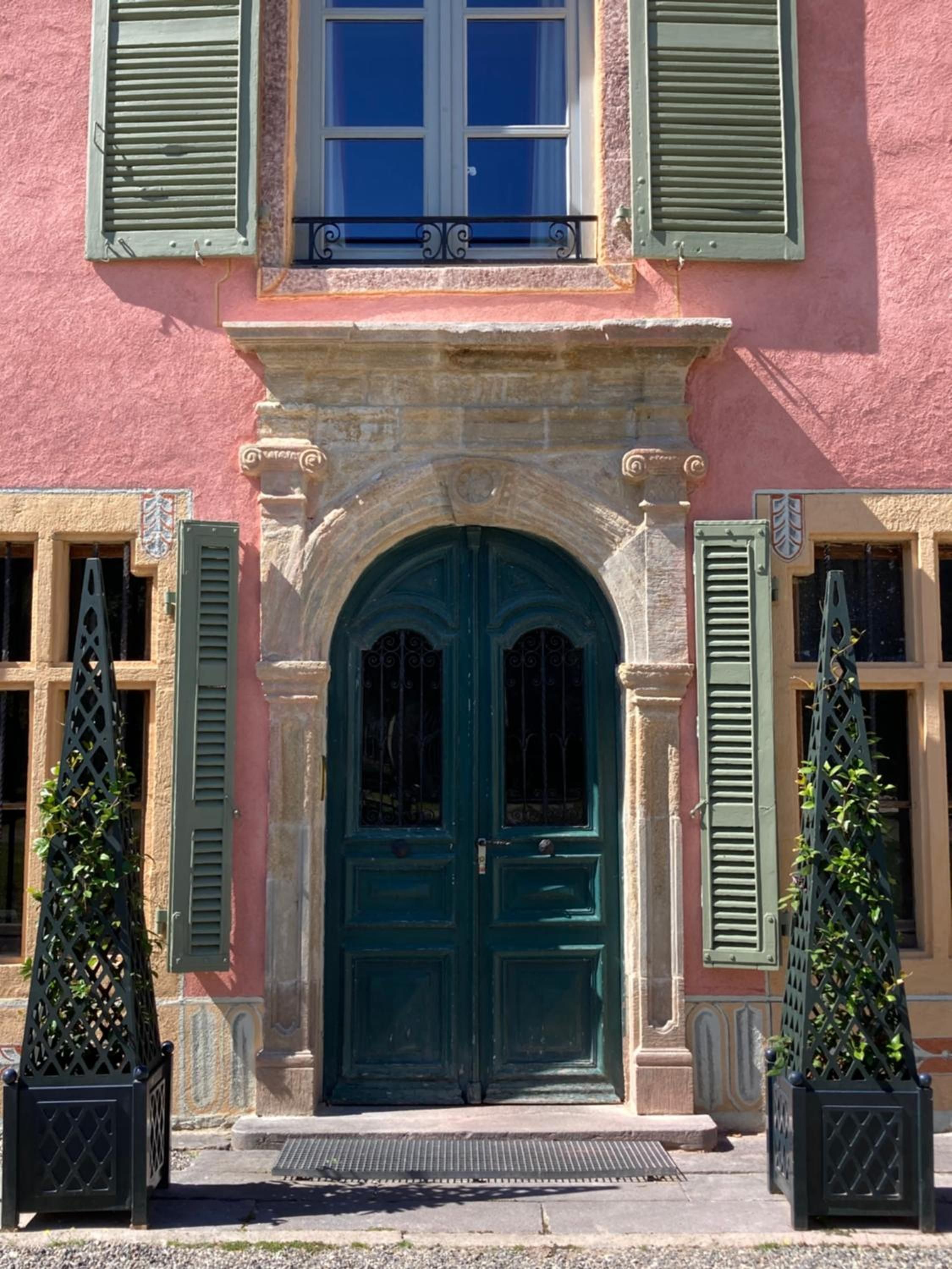 A building with a prominent green door, a balcony with a black balustrade, and two green window shutters.