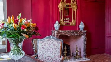 Une pièce avec un mur rouge, une cheminée, un miroir et un arrangement floral sur une table.
