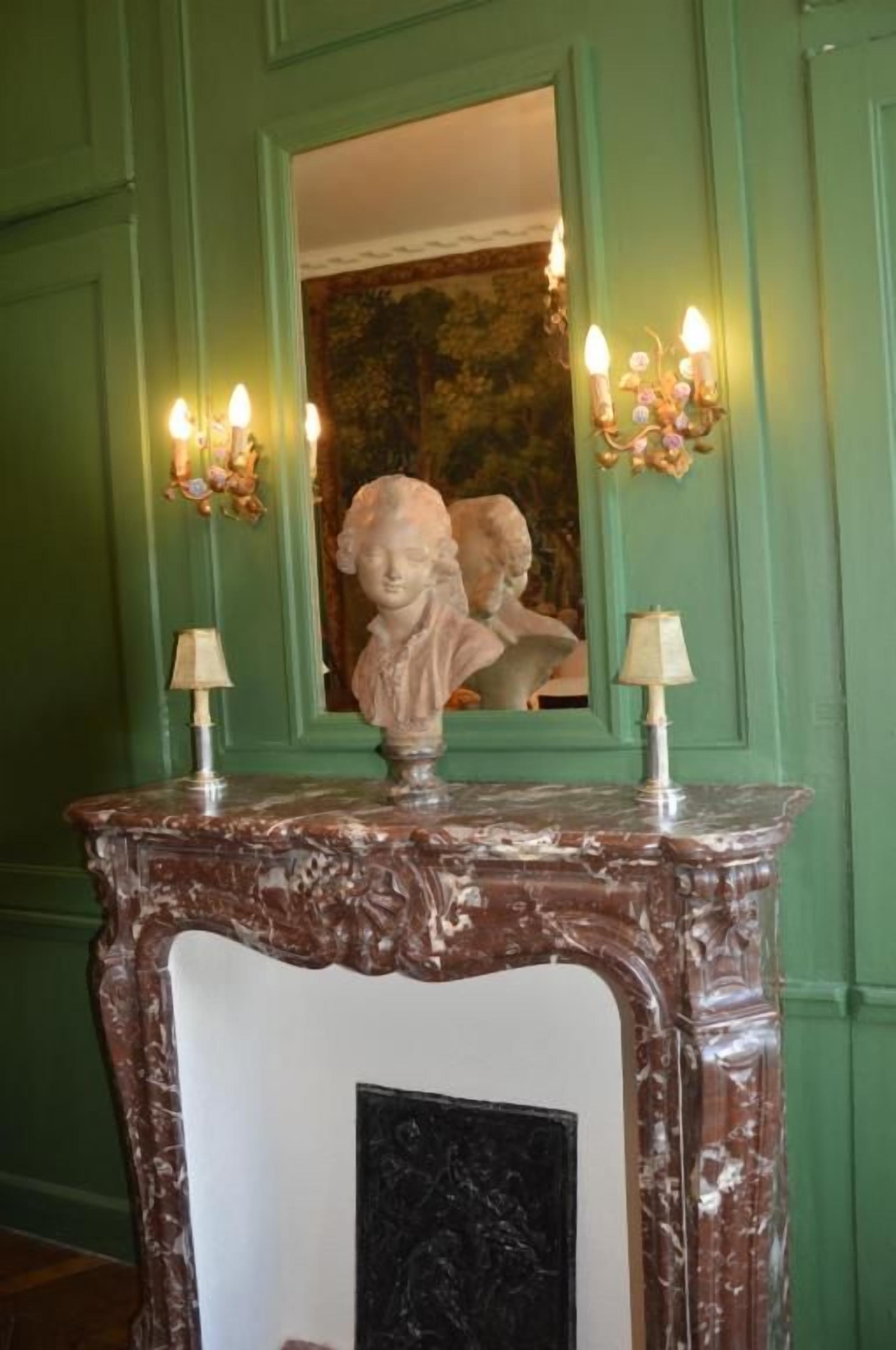Une cheminée en marbre surmontée d’un miroir, avec des appliques murales de chaque côté.