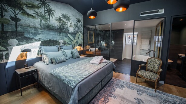A bedroom with a large bed, a nightstand, a chair, a glass door leading to a bathroom, and a mural on the wall. - Domaine de Chalaniat (La Sauvetat)