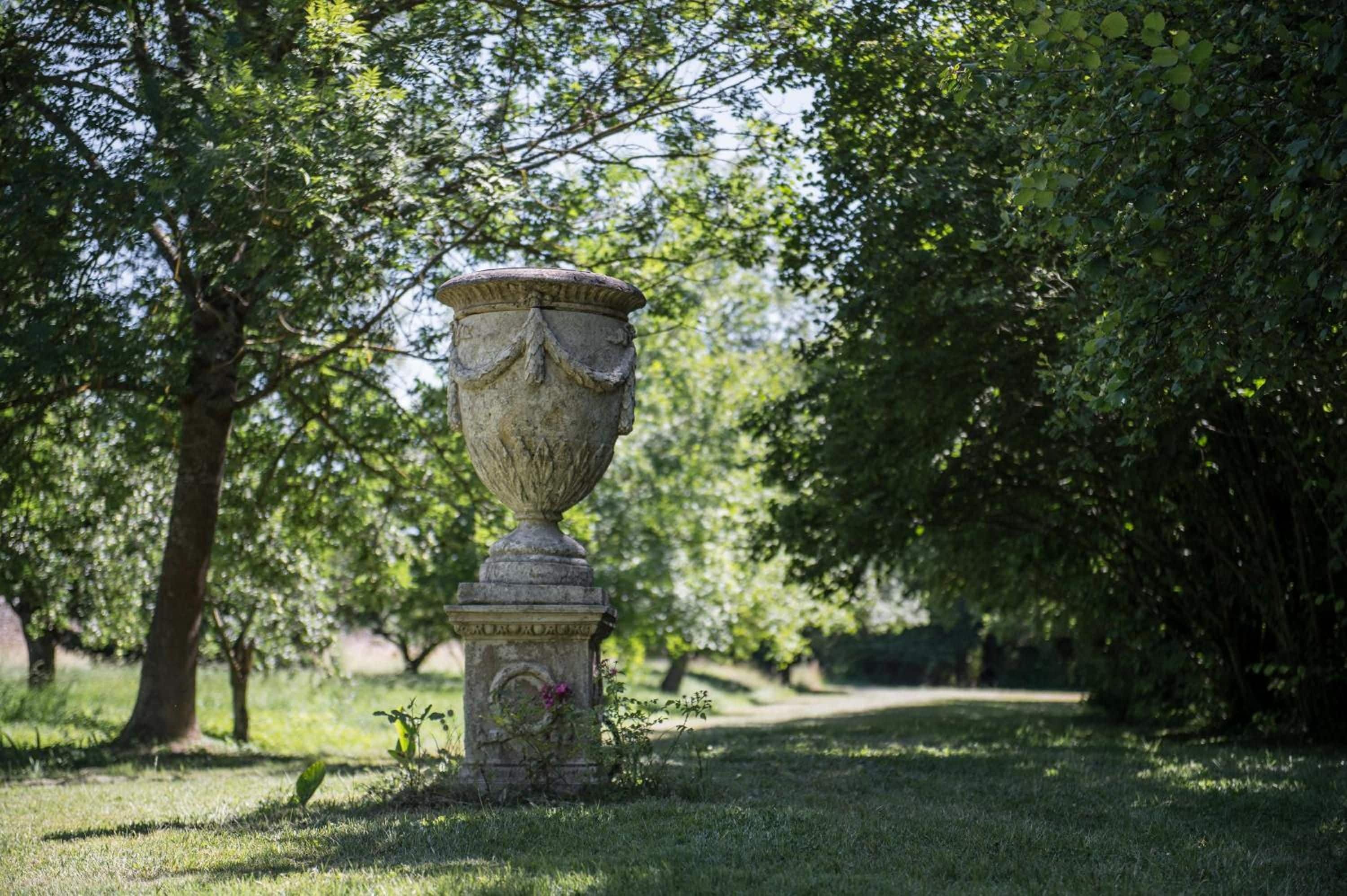 A stone urn on a pedestal in a park with trees and grass.
