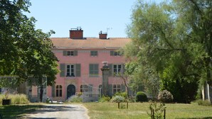 A large, pink building with a red-tiled roof, surrounded by trees and a fence. - Domaine de Chalaniat (La Sauvetat)