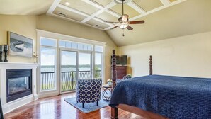 A bedroom with a large bed, a fireplace, a ceiling fan, and a view of a lake through the sliding glass doors. - Minutes from Downtown Cambridge | Private Dock | Pool | Kayaks (Cambridge)