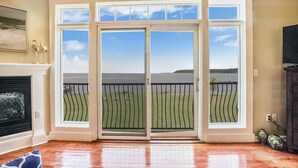 A room with a large sliding glass door leading to a balcony with a view of a lake and grassy area. - Minutes from Downtown Cambridge | Private Dock | Pool | Kayaks (Cambridge)