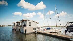 Een drijvend woonschip afgemeerd in een jachthaven, met een heldere lucht en rustig water.