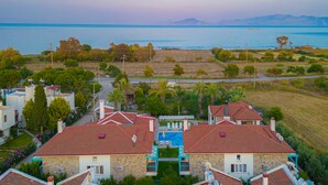 A coastal residential area with houses featuring red roofs and stone walls, a swimming pool, and a view of the sea and distant mountains. - Ekinoks Butik Otel (Datça)