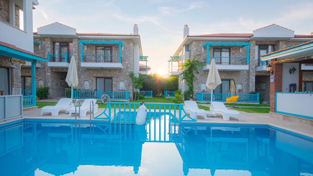 A swimming pool with lounge chairs and umbrellas, surrounded by stone buildings with balconies. - Ekinoks Butik Otel (Datça)