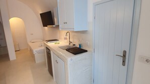 A compact kitchen with white cabinets, a sink, and a door. - Nefeli Traditional Cave Houses (Santorini)