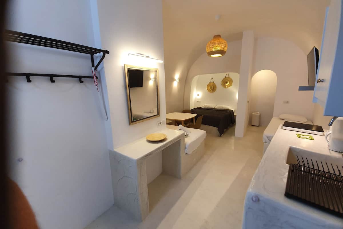Une salle de bain moderne avec un grand miroir, un lavabo et une commode sur laquelle est posée une serviette. On y trouve également un lit avec une tête de lit et une table de chevet sur laquelle se trouvent un livre et une lampe.