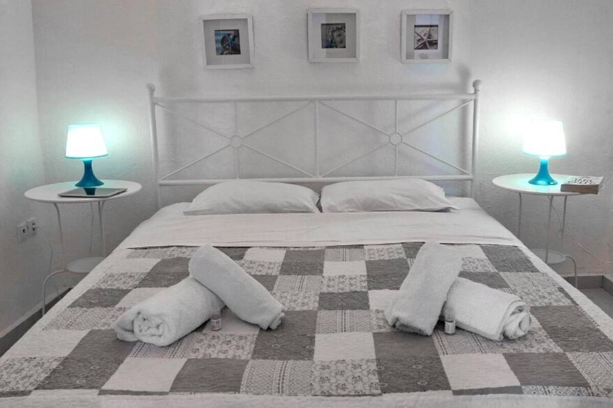 Un lit bien fait, recouvert d’une couverture à carreaux, avec deux lampes de chevet et trois tableaux encadrés accrochés au mur.