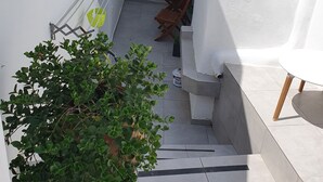 A narrow outdoor corridor with a white door, a small table, and a potted plant. - Nefeli Traditional Cave Houses (Santorini)