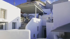 A narrow street with white buildings, a covered staircase, and a small table with chairs. - Nefeli Traditional Cave Houses (Santorini)
