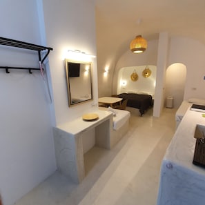 A modern hotel room with a large bed, a small desk, a vanity with a mirror, and a bathroom with a toilet and sink.