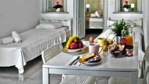 A compact hotel room with two single beds, a small dining table with breakfast items, and a hanging light fixture. - Nefeli Traditional Cave Houses (Santorini)