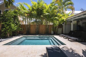 Une piscine rectangulaire entourée d’une terrasse en bois, une clôture en bambou et un patio couvert avec des sièges.