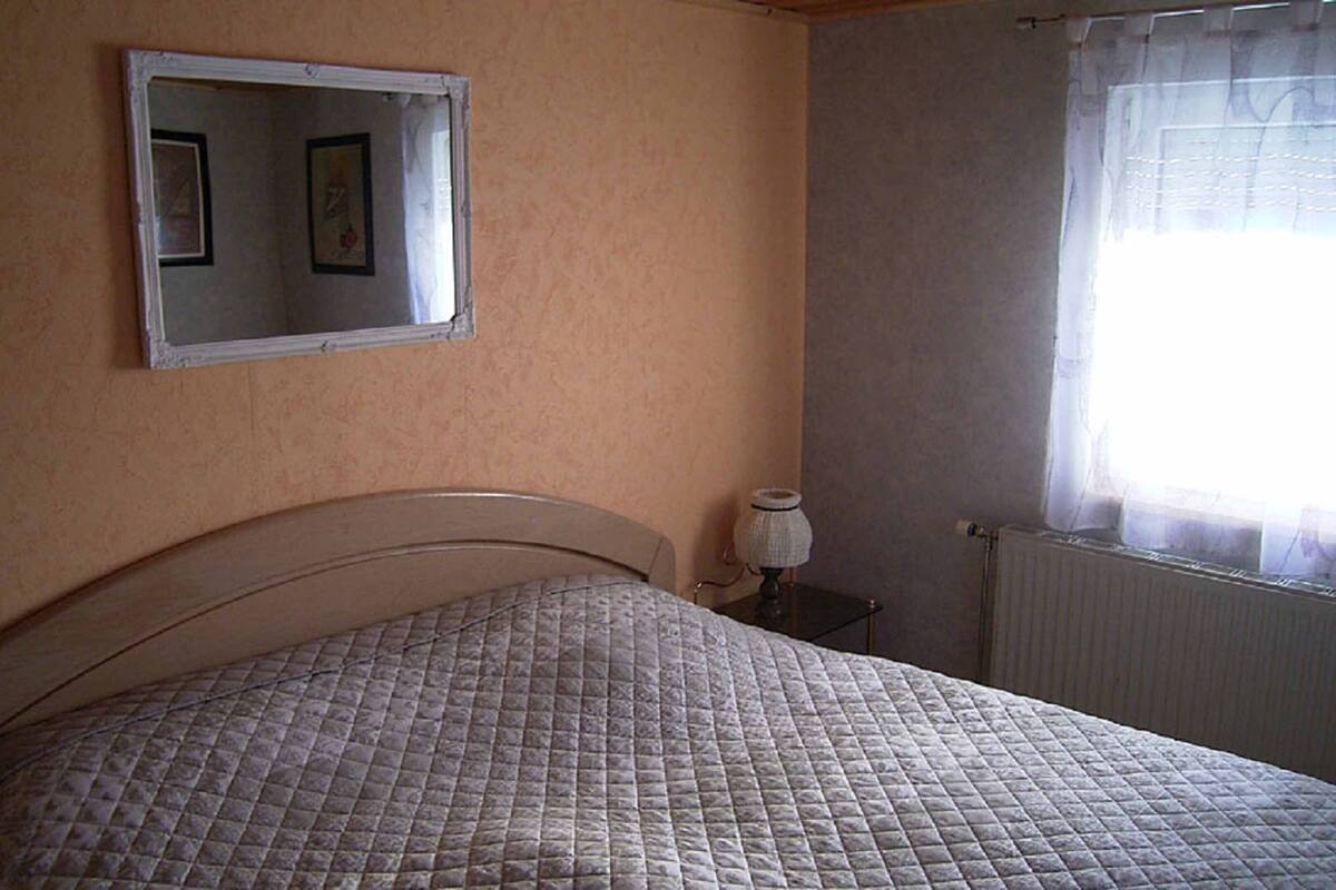 Une chambre à coucher comprenant un lit, une table de chevet, une lampe, une fenêtre avec des rideaux et un miroir fixé au mur.