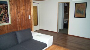 A living room with a grey sofa, wooden walls, and a white door leading to another room. - Naturfreundepension Hagenberger für Erwachsene (Witzmannsberg)
