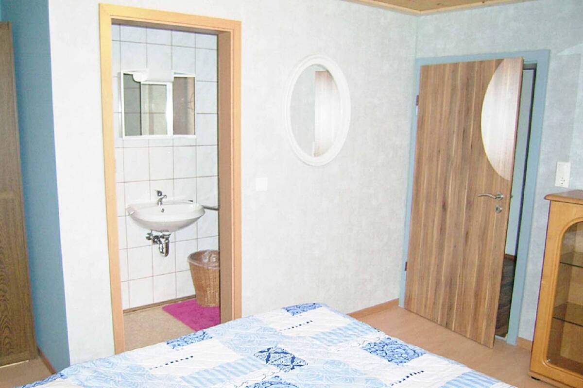 Une chambre à coucher avec un lit, une armoire en bois, une porte en bois, une salle de bain avec un lavabo et un miroir.