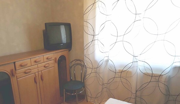 Une pièce avec un meuble en bois, un téléviseur posé dessus, une chaise et un rideau à motifs.